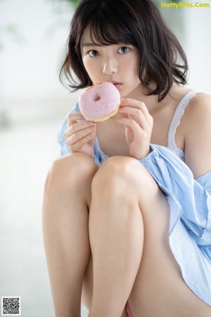 A woman holding a purple donut in front of her eyes.
