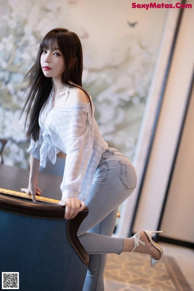 A woman in a white shirt and jeans leaning on a blue chair.