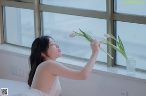 A woman in a white dress sitting on a bed.
