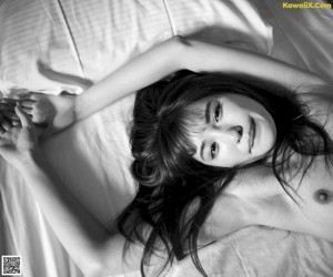 A young woman laying on a bed holding a white sheet.