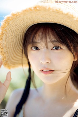 A woman wearing a straw hat standing next to a wall.
