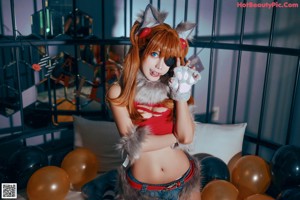 A woman in a red top and furry outfit sitting on a bed.