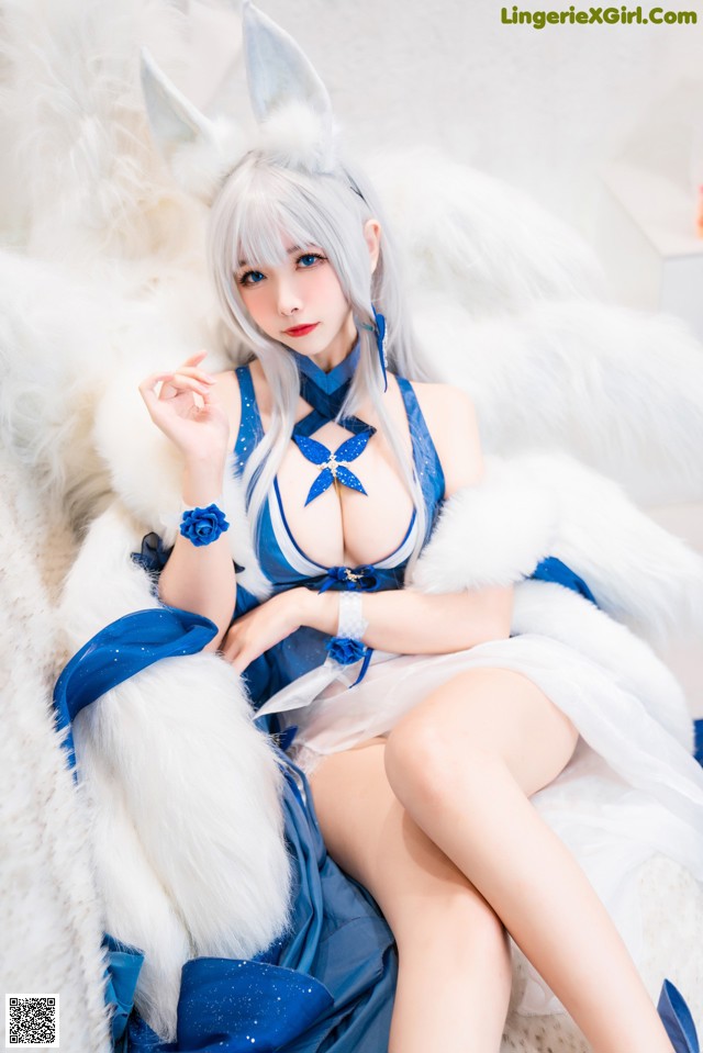 A woman in a blue and white outfit sitting on a white couch.