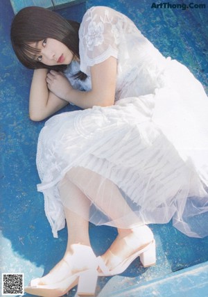 A woman in a white dress sitting on a wooden dock.